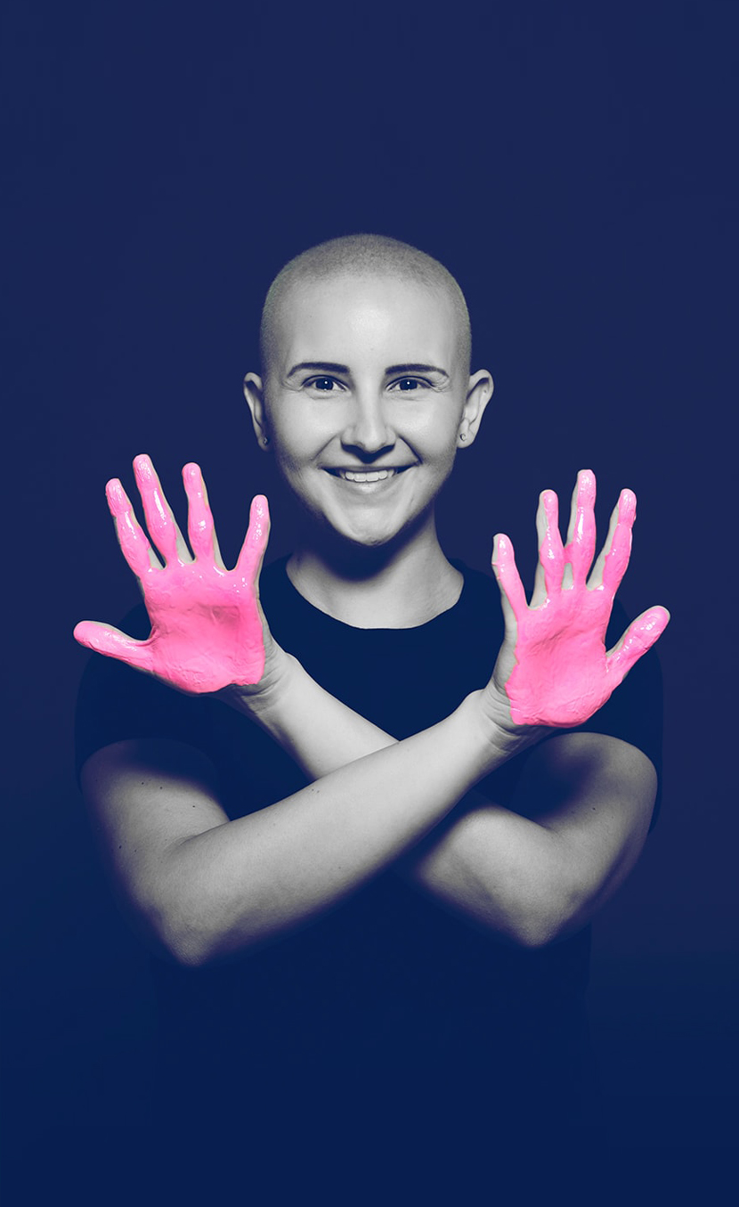 Breast cancer survivor posing for the in our hands healthcare campaign with her arms crossed over her chest, palms facing out, and pink paint on her hands.
