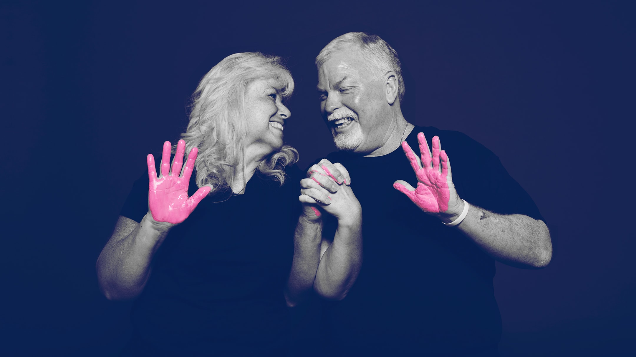 A woman and a man looking at each other and smiling with pink paint on their hands.