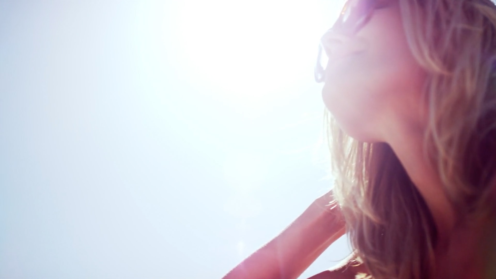 A close up shot of a woman's face from below being almost blocked out from a sun burst.