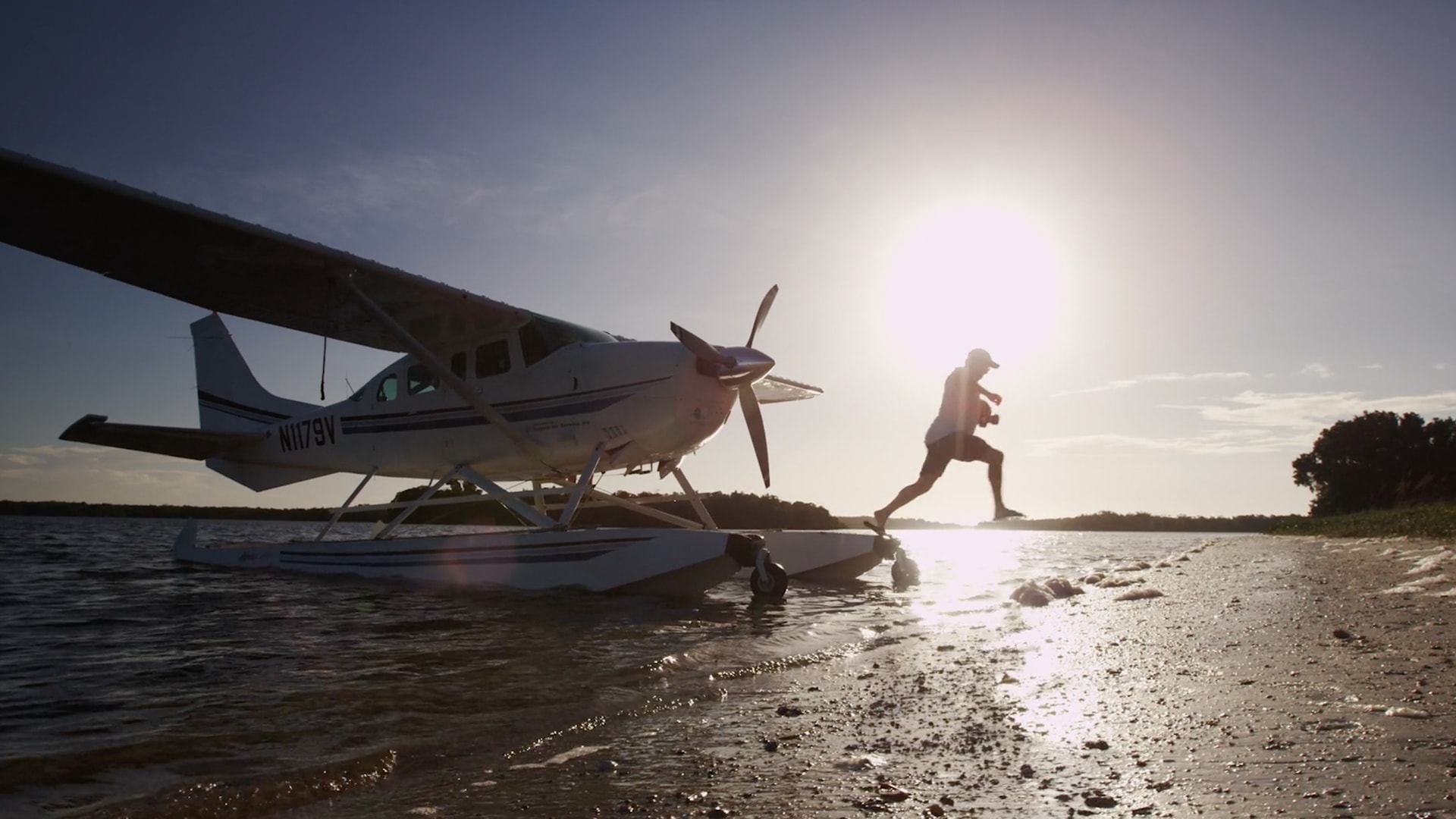 A man jumping onto the beach from a parked seaplane.