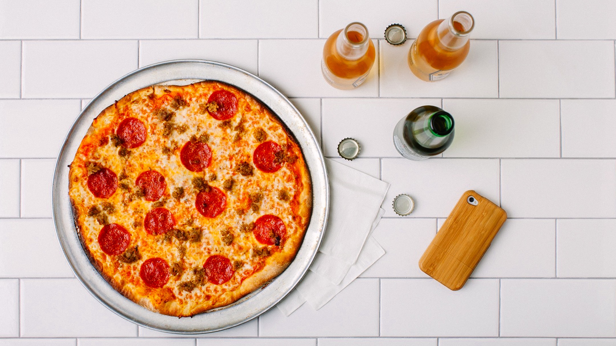 An overhead shot of of Ciccio Cali's pizza with three opened drinks on a white-tiled counter top.